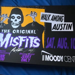 May include: A black and white concert poster for The Original Misfits, featuring a skull-faced character with a yellow background. The poster advertises a concert in Austin, Texas on Saturday, August 10th at the Moody Center. The poster includes the band's name, the date of the concert, and the venue.