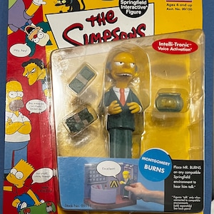 May include: A yellow plastic action figure of Mr. Burns from The Simpsons, wearing a dark suit and red tie. The figure is holding a briefcase and has a yellow background with the words "The Simpsons" and "World of Springfield Interactive Figure".