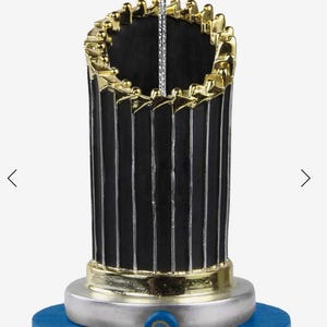 May include: A blue and silver World Series trophy ornament with the Los Angeles Dodgers logo and the text "World Series Champions 2020 LA 2024".