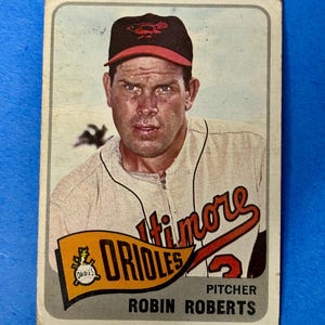 May include: Vintage baseball card featuring Robin Roberts, pitcher for the Baltimore Orioles. The card shows Roberts in his Orioles uniform, with the team logo and name prominently displayed. The card has a worn appearance.