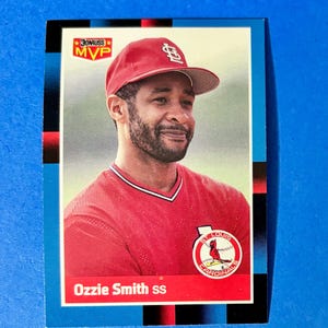 May include: A baseball card featuring Ozzie Smith of the St. Louis Cardinals. The card has a red and white color scheme, with the team logo and the text "St. Louis Cardinals" visible. The card also has the text "Ozzie Smith ss" at the bottom.
