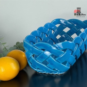 Könnte beinhalten: Ein geflochtener Korb aus türkisblauem Keramik mit einem dekorativen Design. Der Korb steht auf einer schwarzen Oberfläche mit zwei Zitronen daneben.