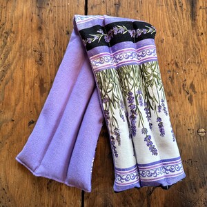 Op de afbeelding: Paarse lavendel-print stoffen warmtekussen met een zachte, pluche paarse voering. Het kussen is ontworpen om te gebruiken als een nek- of schouderwrap.