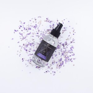 May include: A clear spray bottle with a black cap and a label featuring geometric designs and the text "Ocean Dream Tea". The bottle is surrounded by small, purple and white stones on a white background.