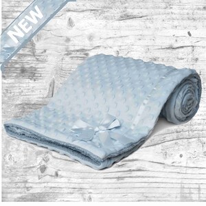 May include: A light blue baby blanket with a white satin ribbon and a bow. The blanket is made of soft, plush fabric and has a textured pattern.