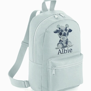 May include: A light grey canvas backpack with a zipped pocket on the front. The backpack has a giraffe design with the name "Albie" embroidered on the front.