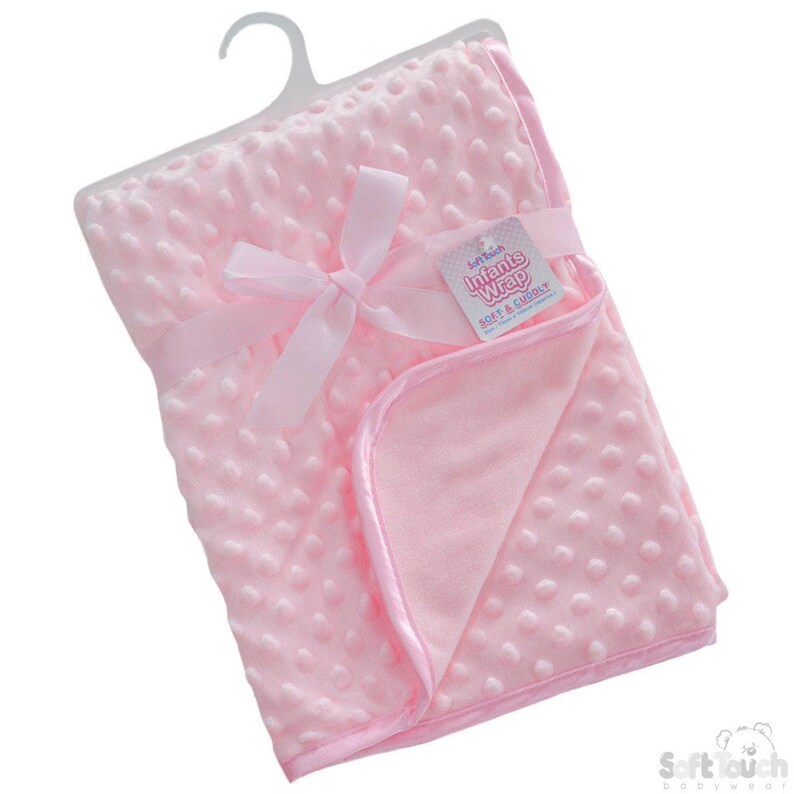 May include: A pink baby blanket with a soft, textured surface. The blanket is tied with a pink ribbon and has a tag that reads "Soft Touch Infants Wrap Soft & Cuddly".