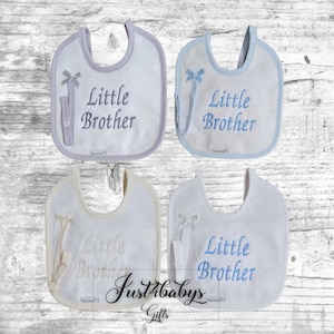 May include: Four white baby bibs with blue trim and a blue bow. Each bib has a pocket for a dummy and says "Little Brother" in blue embroidery.