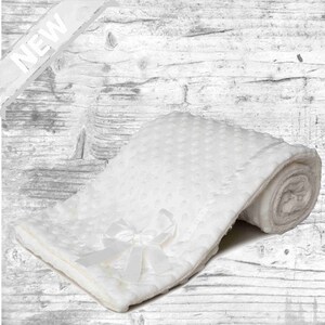 May include: White baby blanket with a satin bow. The blanket is made of soft, plush fabric and has a dotted pattern.