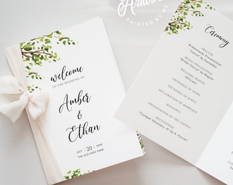 May include: Wedding stationery set featuring a welcome card with the names "Amber & Ethan" and a program with ceremony details. The cards have a white background with green floral accents and a cream ribbon.