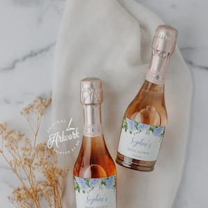 Könnte beinhalten: Zwei Mini-Flaschen Roséwein mit personalisierten Etiketten für eine Brautparty. Die Etiketten zeigen ein Aquarelldesign mit blauen Hortensien und dem Text "Sophia's Bridal Shower".