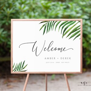 May include: A white welcome sign with a tropical leaf design. The sign reads "Welcome Amber + Derek July 31th - 20XX - Key West"