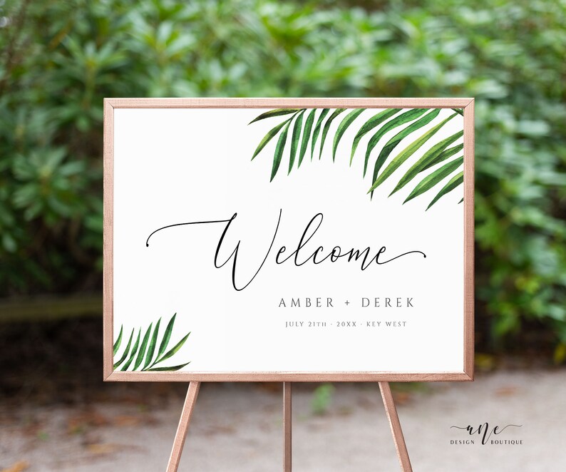 May include: A white welcome sign with a tropical leaf design. The sign reads "Welcome Amber + Derek July 31th - 20XX - Key West"