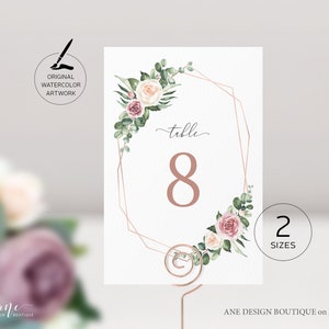 May include: A white table number card with a gold geometric frame and watercolor floral design. The card says "table 8" in a pink font.