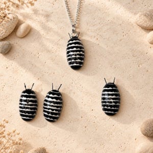 May include: A silver chain necklace with a pendant shaped like a pill bug, featuring a glossy black finish with horizontal white stripes. Three additional matching pill bug charms are arranged below the necklace pendant.