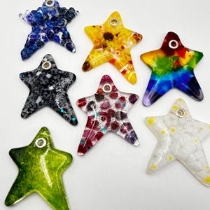 May include: Eight glass star-shaped ornaments with different designs and colours. The stars are all about 7.5 cm in diameter and have a silver loop for hanging.