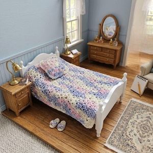 May include: A miniature bedroom scene with a white bed frame, a crocheted blanket in pastel colors, and a matching pillow. The room includes wooden nightstands with lamps, a dresser, and a small rug. The scene is a dollhouse bedroom.