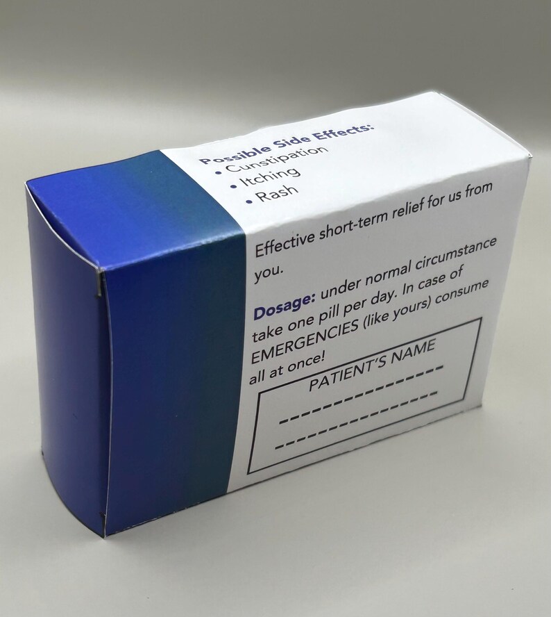 Op de afbeelding: Een blauwe en witte doos met de tekst "Possible Side Effects: Constipation, Itching, Rash" en "Dosage: onder normale omstandigheden &eacute;&eacute;n pil per dag innemen. In geval van NOODGEVALLEN (zoals die van u) alles in &eacute;&eacute;n keer innemen!" De doos heeft ook een lege ruimte voor de naam van de pati&euml;nt.