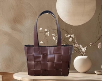 May include: A brown woven tote bag with a square shape and two handles. The bag is sitting on a wooden table.