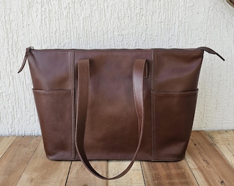 May include: A brown leather tote bag with two top handles and a zip closure. The bag has a front pocket and a back pocket.