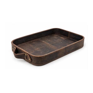 Puede incluir: Una bandeja rectangular de cuero marrón oscuro con acabado desgastado, bordes elevados y un asa única en el lado izquierdo asegurada con remaches metálicos. La base interior muestra un patrón de costura en cruz que divide la superficie.