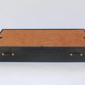 Puede incluir: Una bandeja rectangular con un marco exterior negro y una base interior de color tostado. La bandeja incluye dos asas negras en los laterales, cada una asegurada con remaches met&aacute;licos de color lat&oacute;n, y una superficie plana y lisa.