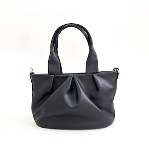 May include: A black leather handbag with a top handle and a shoulder strap. The bag has a pleated design and a smooth finish.