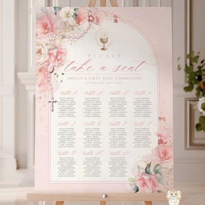 May include: A pink seating chart on a wooden easel, decorated with floral arrangements and the text "Please take a seat." The chart is for Amelia's First Holy Communion and includes a list of names. A cross and chalice are also visible.