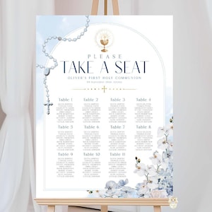 May include: A white sign on a wooden easel with the text "PLEASE TAKE A SEAT" and "Oliver's First Holy Communion". The sign has a blue watercolor background, a rosary, and floral accents. Table assignments are listed below.