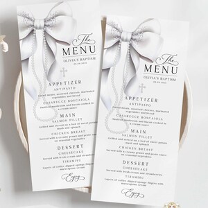 Peut inclure: Deux menus blancs élégants pour le baptême d'Olivia, avec un nœud et un chapelet. Les menus présentent des plats tels que des entrées, des plats principaux et des desserts. Les cartes sont posées sur une assiette blanche.