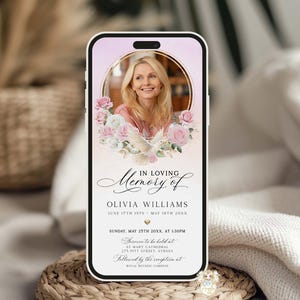 May include: A smartphone displays a memorial invitation. The screen features a photo of a woman surrounded by pink roses and doves. Text reads "In Loving Memory of Olivia Williams" with event details. The phone rests on a woven coaster.
