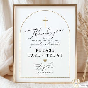 以下が含まれることがあります： 金色のアクセントとエレガントな筆記体で縁取られた洗礼のサイン。サインには「私の洗礼を特別で甘くしてくれてありがとう。お菓子をどうぞ」と書かれています。「オリバー・ブラウン」の名前と日付08.08.2026が含まれています。