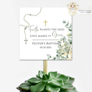 Puede incluir: Una tarjeta blanca con letras doradas y un diseño de eucalipto verde. La tarjeta dice "Faith plants the seed, love makes it grow, Oliver's Baptism, 05/25/2025". Una pequeña cruz dorada y una cadena de cuentas blancas están en la tarjeta.