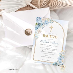 May include: Baptism invitation with a gold cross and floral accents in shades of blue and white. The invitation is accompanied by a white envelope sealed with a gold wax stamp. The invitation is on a white surface.