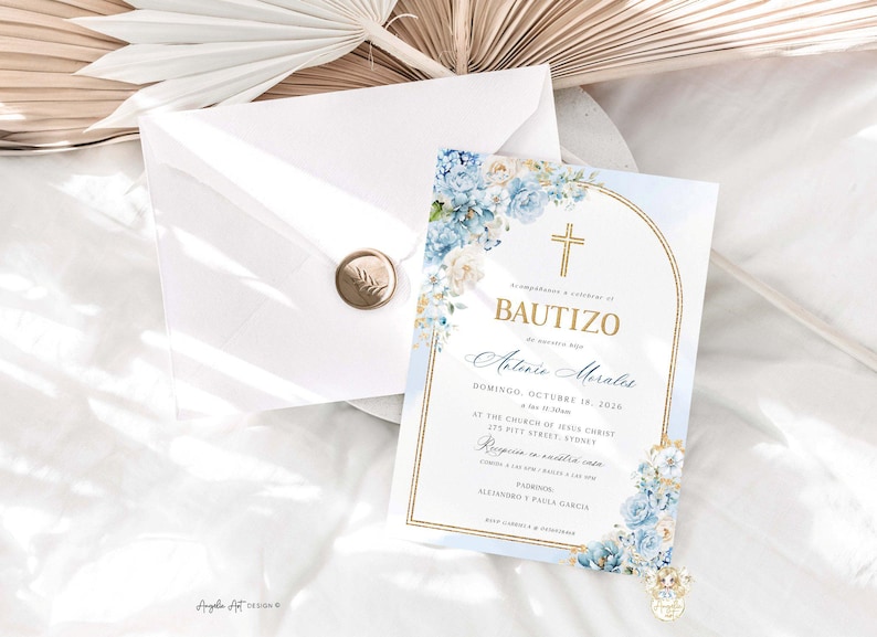 May include: Baptism invitation with a gold cross and floral accents in shades of blue and white. The invitation is accompanied by a white envelope sealed with a gold wax stamp. The invitation is on a white surface.