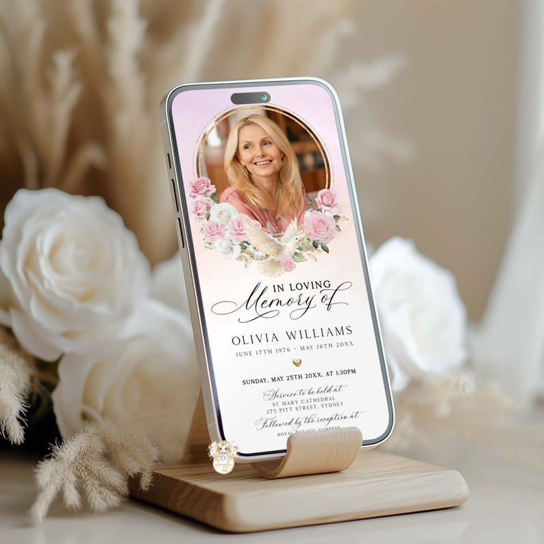May include: A smartphone displays a memorial graphic with the text "In Loving Memory of Olivia Williams." The design features a photo, floral accents, and event details. The phone rests on a wooden stand, with soft floral and neutral background.