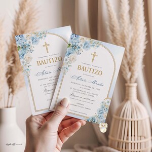 May include: Two baptism invitations with floral and gold accents. The cards feature a cross, the word "BAUTIZO", and event details. The design includes blue and white flowers, with text in gold and blue.