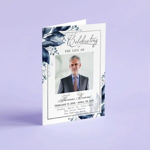 May include: A white memorial card with a blue watercolour floral design. The card features a photo of a man in a suit and tie. The text reads "Celebrating the Life of Thomas Evans, February 15, 2010 - April 20, 2110. Sunday, April 25, 2110, 10am, The Local Church, The Address Here."