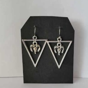 May include: Silver triangle earrings with a silver ram head charm hanging from each triangle.