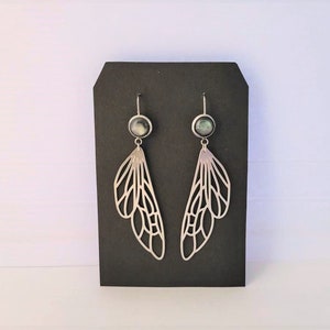 May include: A pair of silver dangle earrings with a black and white iridescent stone at the top and a delicate silver wing design.