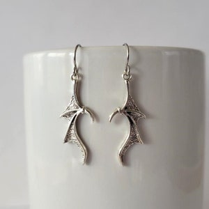 May include: A pair of silver dangle earrings with a wing design. The wings are detailed and have a textured finish.