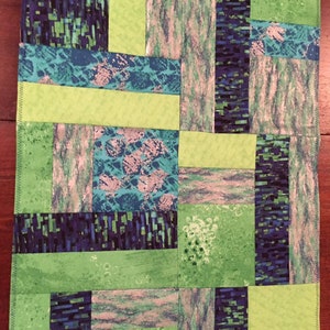 Puede incluir: Una colcha de retazos verde y azul con un patr&oacute;n geom&eacute;trico. La colcha est&aacute; hecha de diferentes telas con varias texturas y colores.