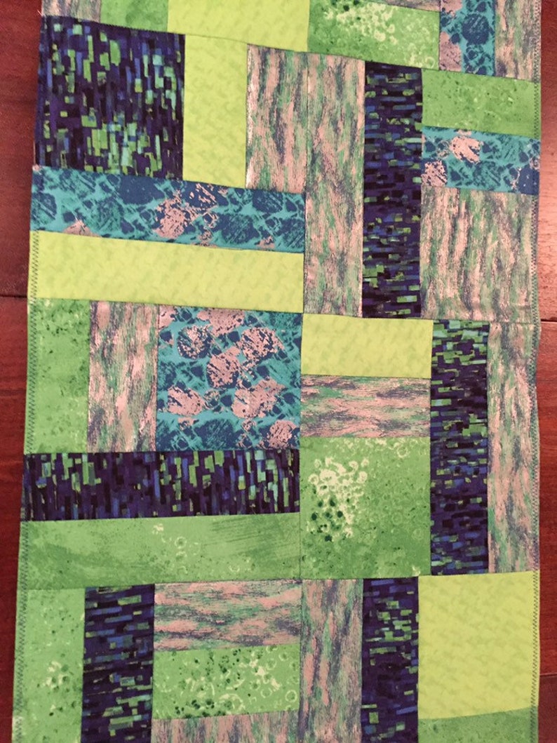 Puede incluir: Una colcha de retazos verde y azul con un patr&oacute;n geom&eacute;trico. La colcha est&aacute; hecha de diferentes telas con varias texturas y colores.