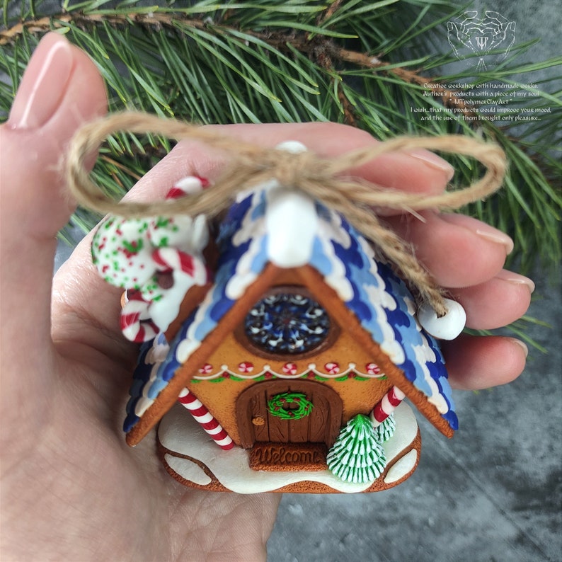 May include: A miniature gingerbread house Christmas ornament with blue and white icing, candy canes, a wreath on the door, and the word "Welcome" on the front.