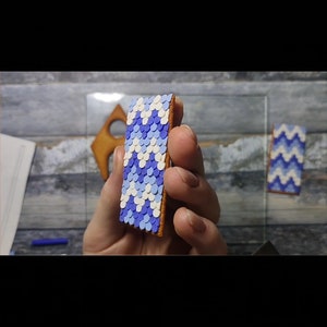 May include: A close-up of a rectangular cookie decorated with a blue and white geometric pattern. The cookie is held in a hand.
