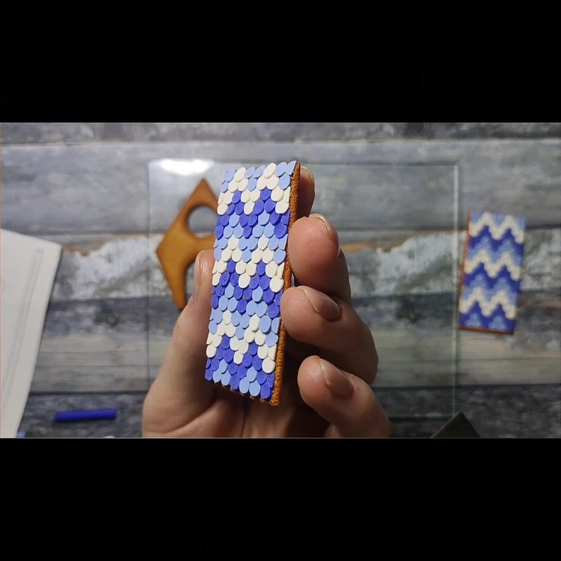 May include: A close-up of a rectangular cookie decorated with a blue and white geometric pattern. The cookie is held in a hand.
