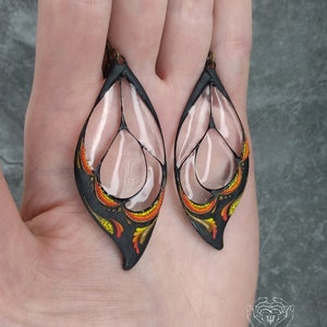 May include: A pair of black and white leaf-shaped earrings with orange, yellow, and red details. The earrings are made of polymer clay and have a delicate, intricate design.