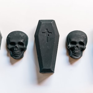 May include: Five black coffin-shaped soaps with a cross design and three black skull-shaped soaps.