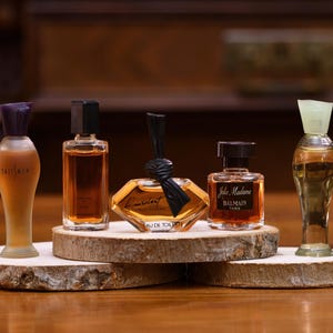 K&ouml;nnte beinhalten: F&uuml;nf Miniatur-Parf&uuml;mflaschen in verschiedenen Formen und Farben werden auf Holzscheiben pr&auml;sentiert. Die Flaschen haben unterschiedlich farbige Fl&uuml;ssigkeiten und Verschl&uuml;sse. Die Flaschen sind auf einer Holzoberfl&auml;che angeordnet.