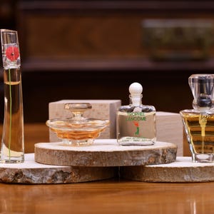 K&ouml;nnte beinhalten: Vier Parf&uuml;mflaschen in verschiedenen Formen und Gr&ouml;&szlig;en werden auf Holzplattformen pr&auml;sentiert. Die Flaschen sind klar, mit bernsteinfarbenen und roten Fl&uuml;ssigkeiten. Eine Flasche hat eine rote Blume oben, und eine andere hat den Text "Trophe Lancome".